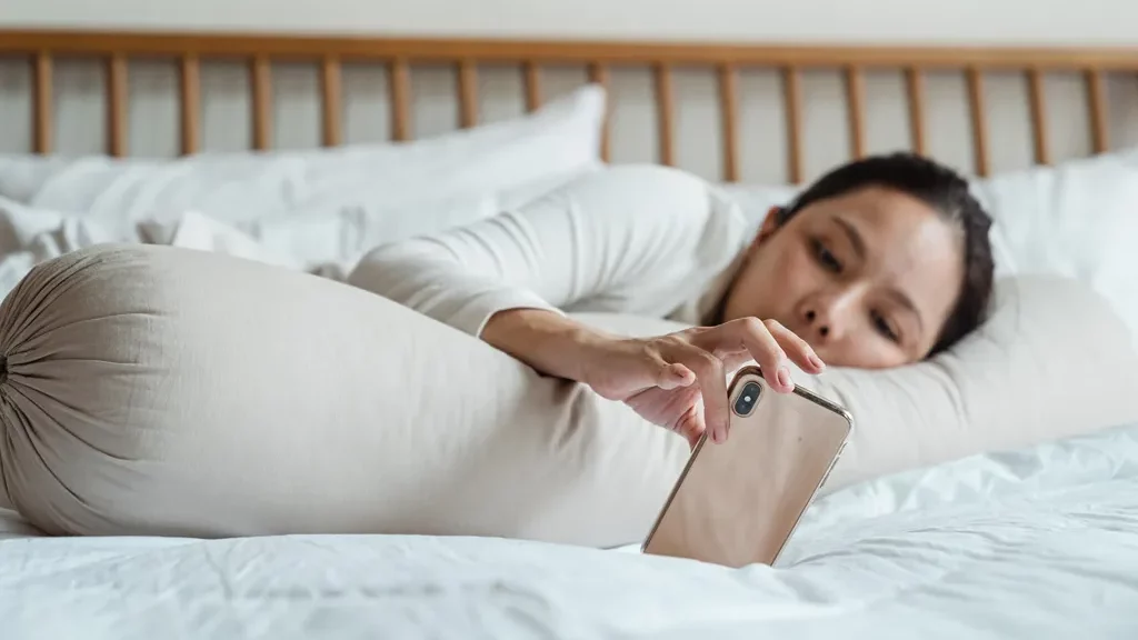 Wanita menggunakan smartphone di tempat tidur