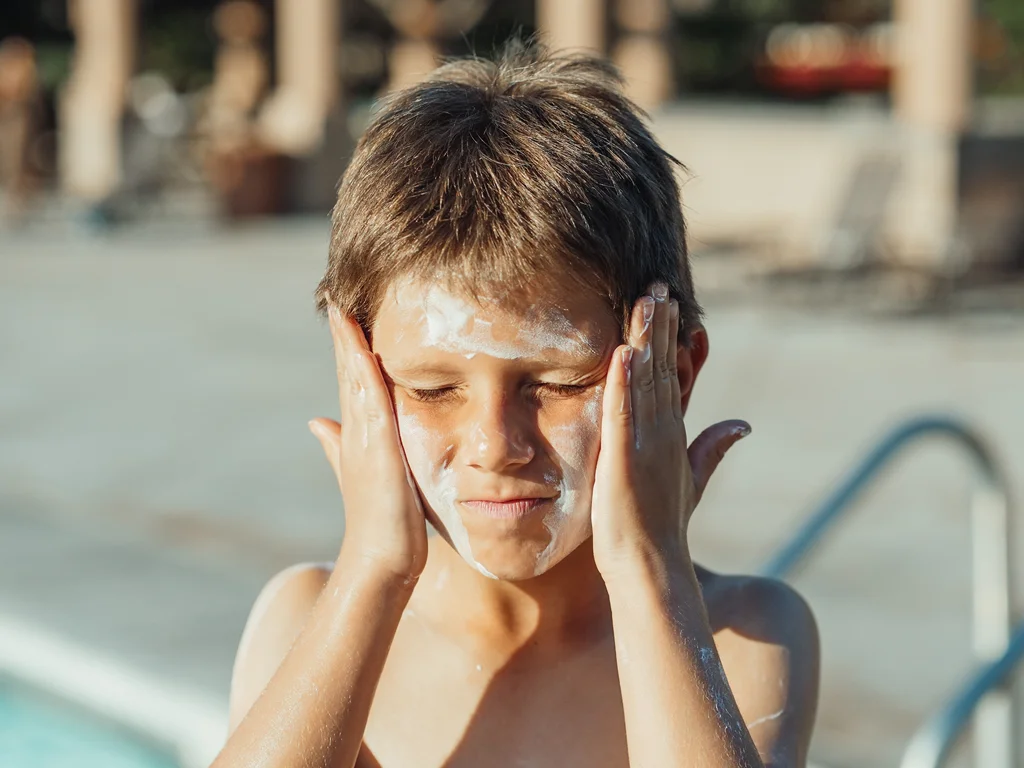 Seorang anak mengoleskan sunblock di wajahnya.