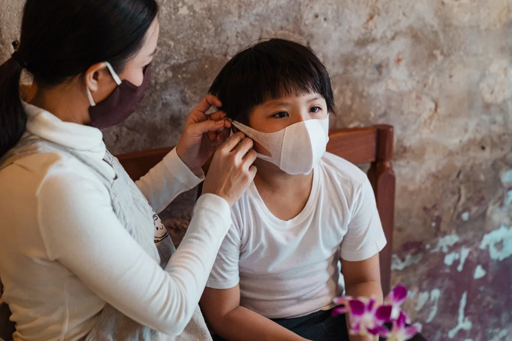 seorang wanita memasangkan masker medis ke seorang anak